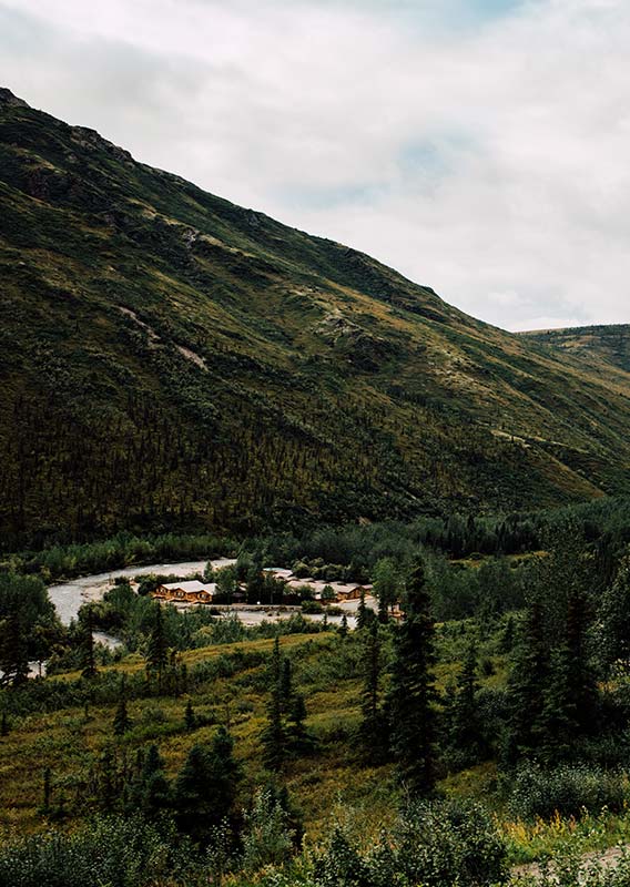 An aerial view of the Denali Backcountry Lodge, nestled alongside a river below forested mountains