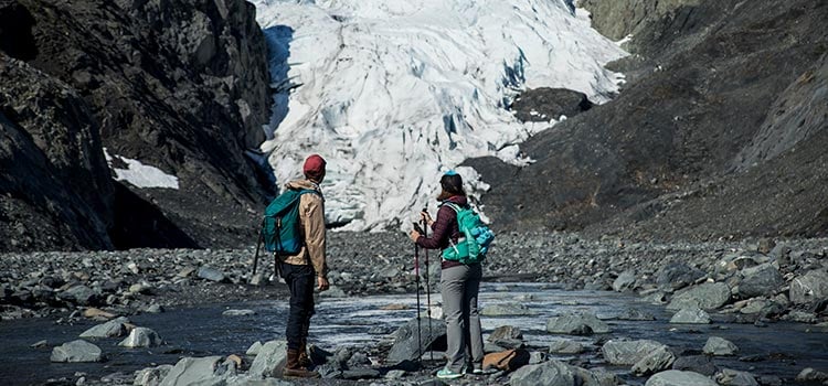 Two hikers observe the Exit Glacier at the base of a drainage