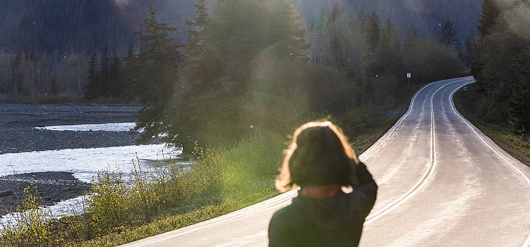 A woman stands on the side of a road shielding her eyes from the sun