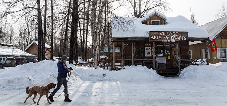 A woman walks a dog by an arts and crafts cabin