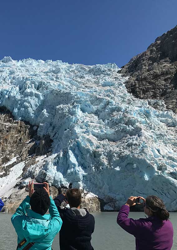 Several sightseers take pictures at the shore of a glacier