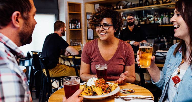 A group of friends sit at a table enjoying beer and nachos