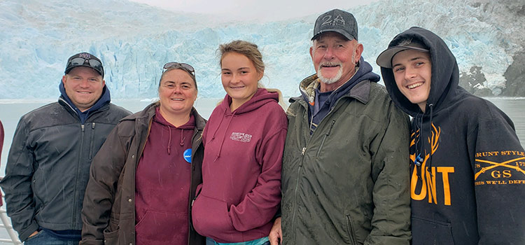 A group of adults and teenagers pose together with a glacier in the background