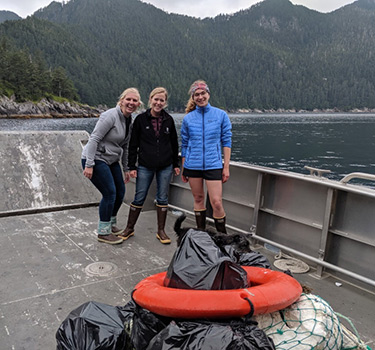 Three women stand on a boat proud of their cleanup efforts
