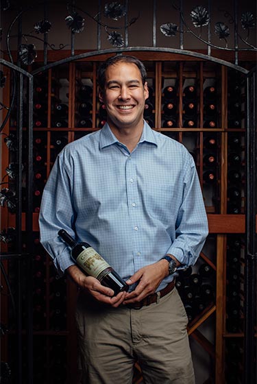 A man smiles in front of a wine cellar.