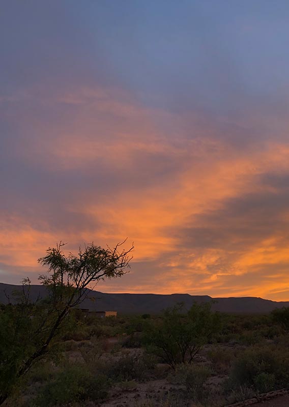 An orange sunset beyond desert mountains.