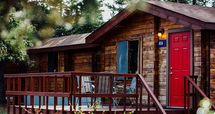 A wooden cabin with a nice deck under conifer trees.