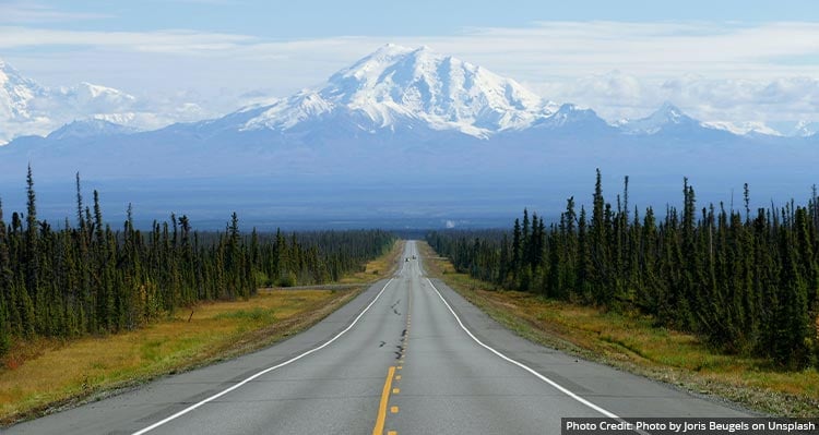 A view down a road towards a tall snow-covered mountain.