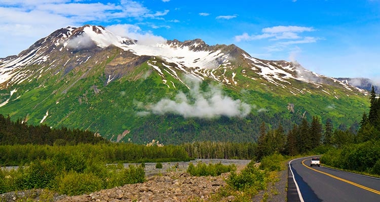 A view down an empty road towards a forest-covered mountain.