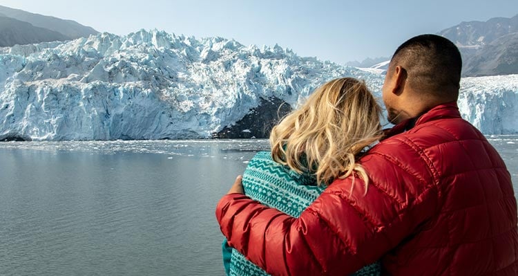 Two people look out towards a seaside glacier.