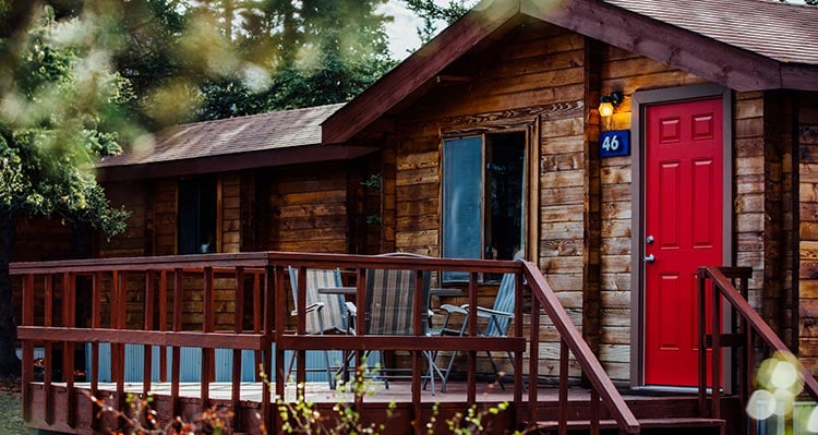 A wooden cabin with a nice deck under conifer trees.