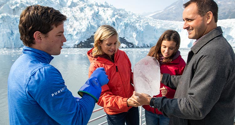 A tour guide shows glacier ice to people on a boat cruise.