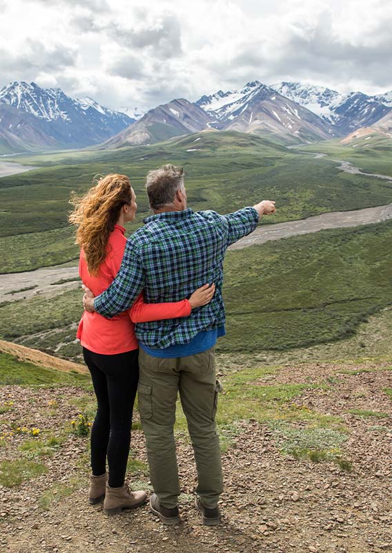 Two people stand at a viewpoint looking towards an open tundra landscape.