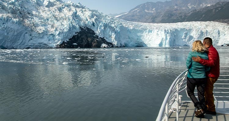 Two people look out to a tidewater glacier from a boat deck.