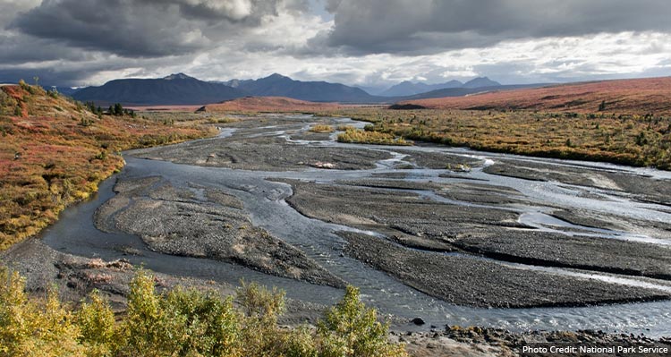 A view down a braided river and floodplain below tall mountains.