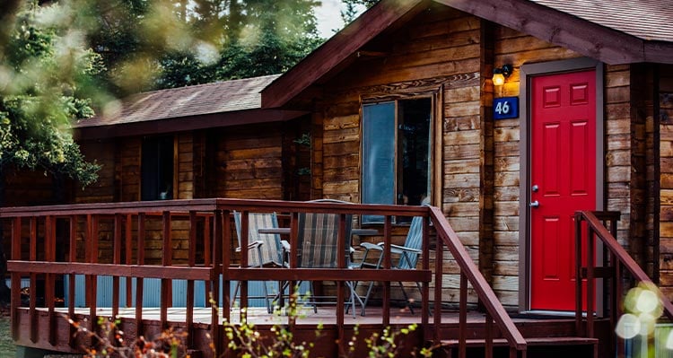 A wood cabin with a bright red door amongst the woods.