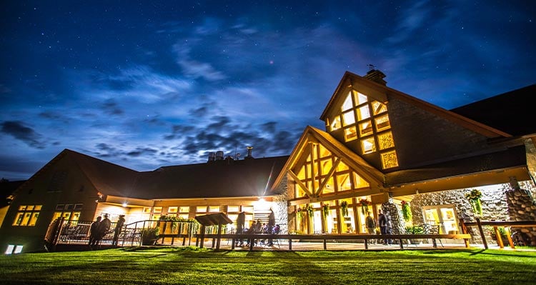 A hotel is lit up at night, people stand outside of the building.