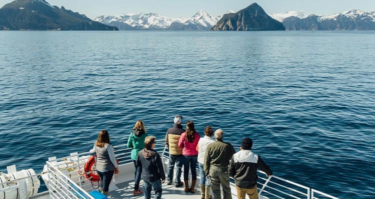 People stand at the edge of a boat looking out to the mountains in the distance.