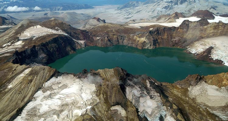 A turquoise blue lake nestled around mountains and snow.