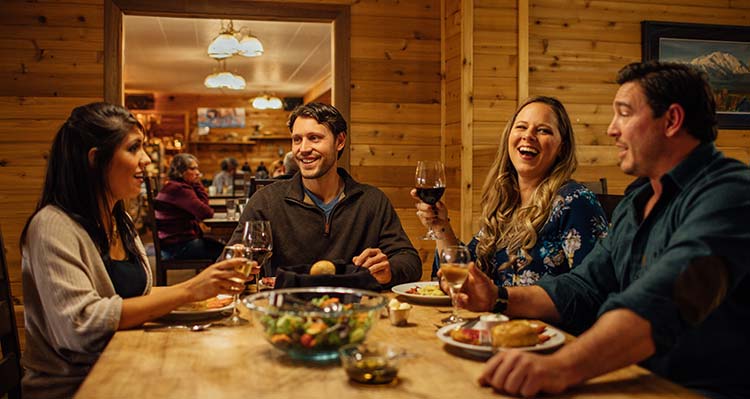 A group of friends dine and  drink inside a wooden wall room.