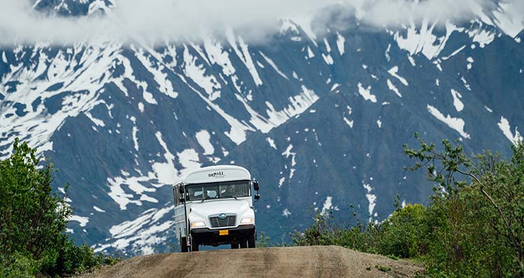 A bus rounds a corner along a mountainside road.