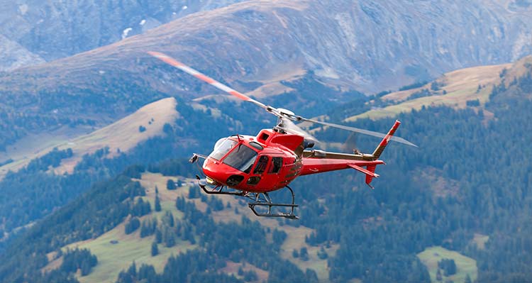 A red helicopter flies in front of mountains.