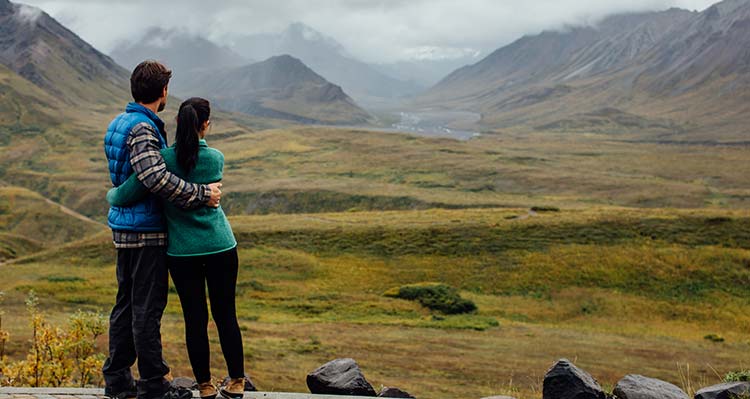 A couple embrace and look out at misty mountains.