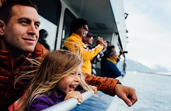 A little girl and her father lean against the edge of a KFT boat.