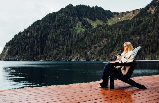 A woman sits in an Adirondack chair on a wooden deck.