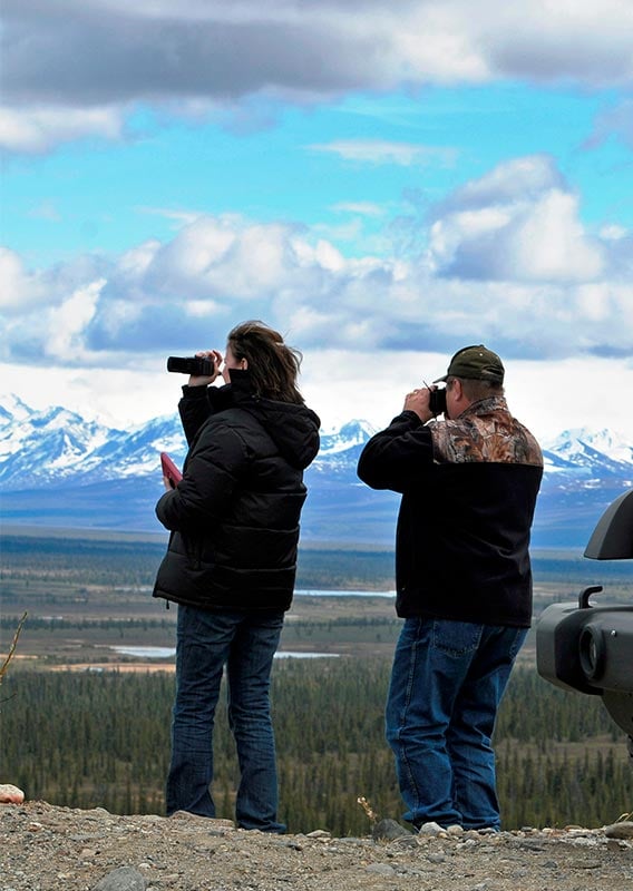 Two people look out from a viewpoint next to a yellow SUV.