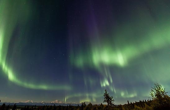Green northern lights are see in the sky above a mountain range in the distance.