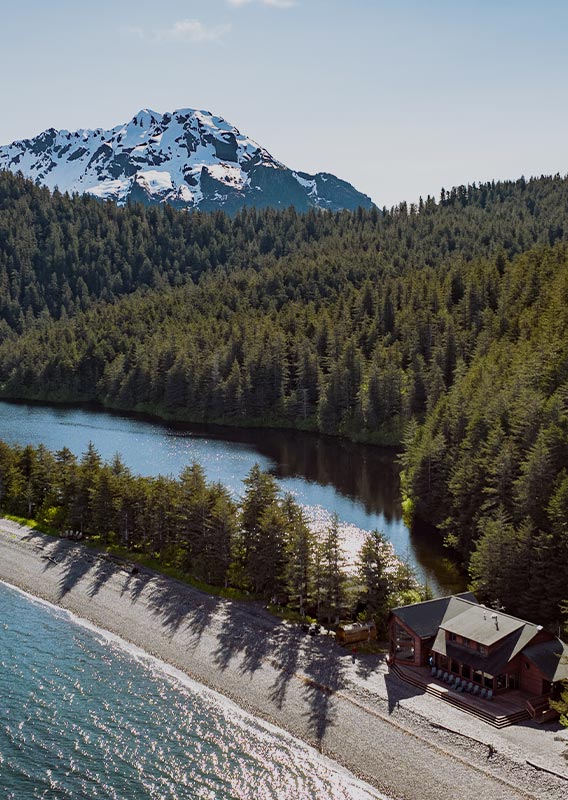 A dock stretches from a spit of land on a forested island among mountains