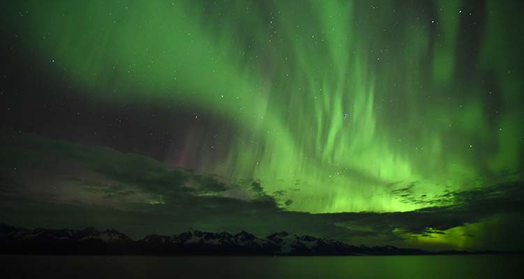 Large green aurora in the night sky, reflected in water.
