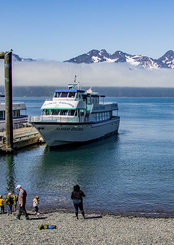 People on a shore while a Kenai Fjords Boat is docked closeby.