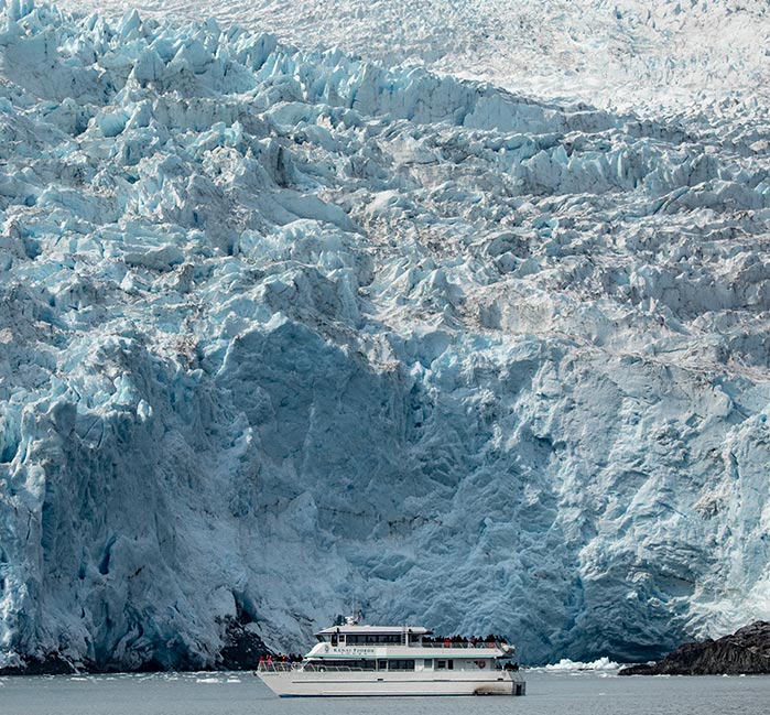 A Kenai Fjords Tours boat in front of a large ice wall.