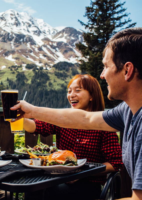 A group of people dining outside and raising glasses in front of a mountain view.