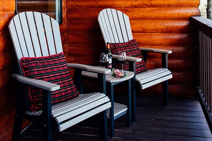 Two Adirondack chairs placed on a balcony of a cabin