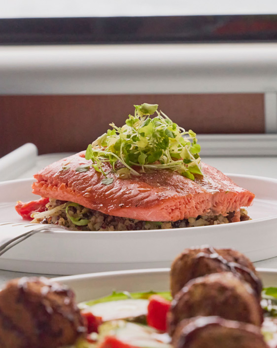 Salmon and meatball entrees set on a table next to a window on a boat.