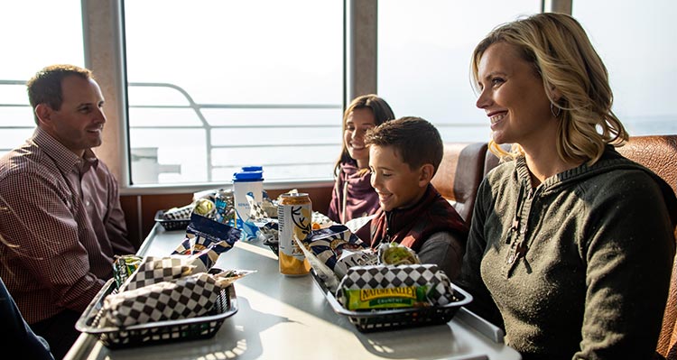 A family sits at a windowside table with dinner trays.