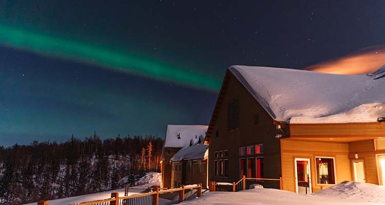 Talkeetna Alaskan Lodge at night with a green aurora behind it.