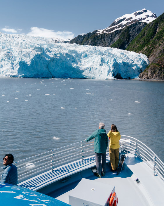 A couple standing on the bow of a KFT boat, looking at Holgate Glacier.