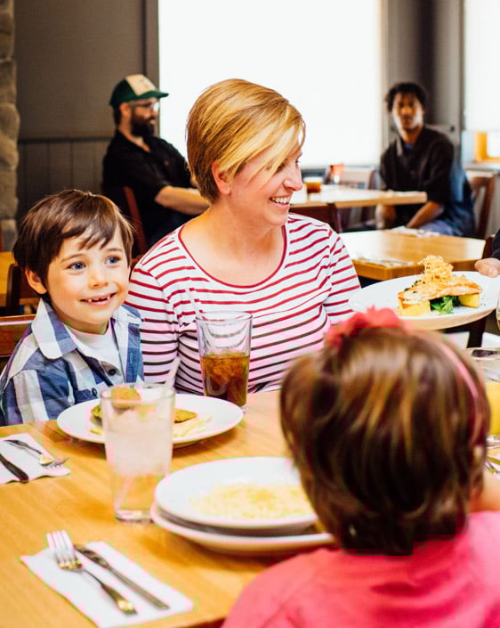 A family laughing over dinner at Prey Pub & Eatery, with guests in the background.