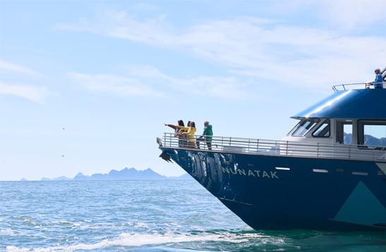 A group of people standing on the bow of a KFT boat, pointing at something in the distance.