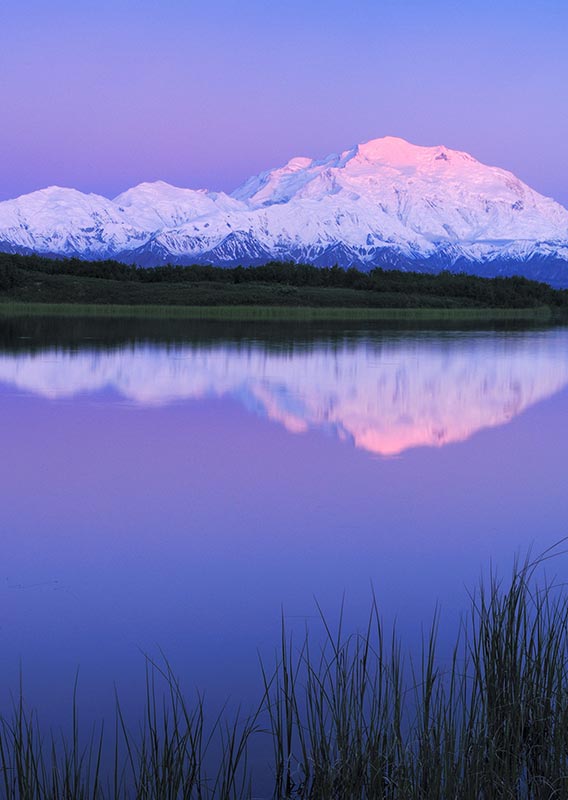 A calm lake below a tall snow-covered mountain.