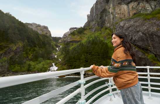 A boat cruising on the sea past a forested cliffside shore.