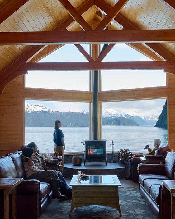 The lounge of a wooden lodge with a large window overlooking the ocean.