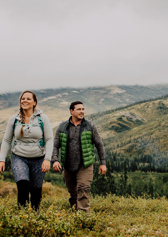 Two people walk on a shrub-covered field.