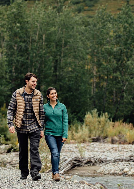 Two people walking on a pebble pathway by a river.