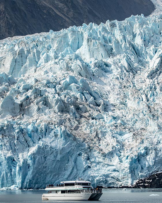 A sightseeing boat below a massive tidewater glacier.