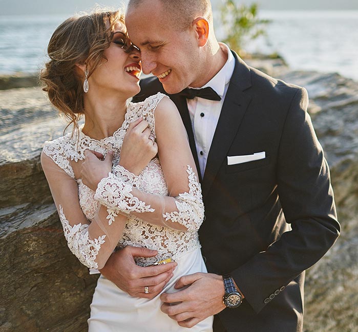 A bridge and groom laugh while on a shoreline.